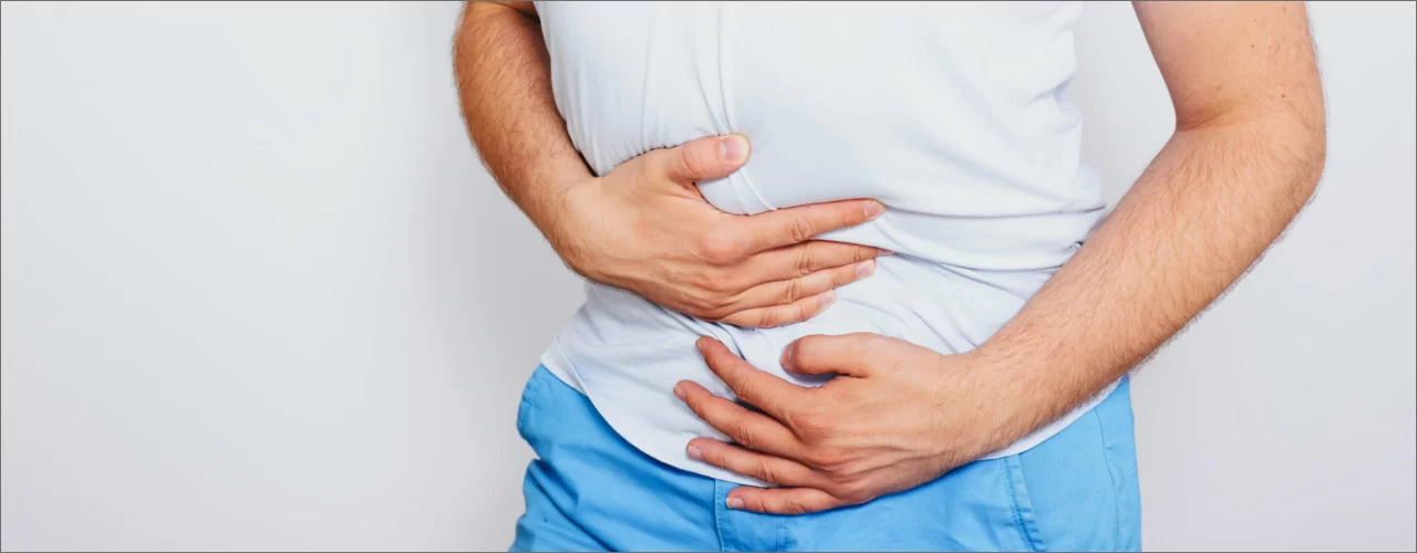 Male patient standing while holding his lower abdomen in both hands indicating pelvic pain.
